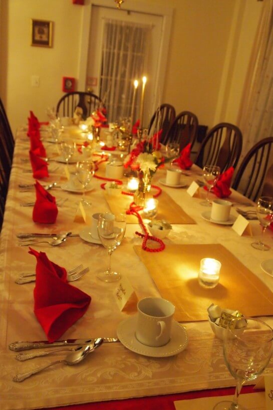 Long dining table set in white with red accents and candlelight. 