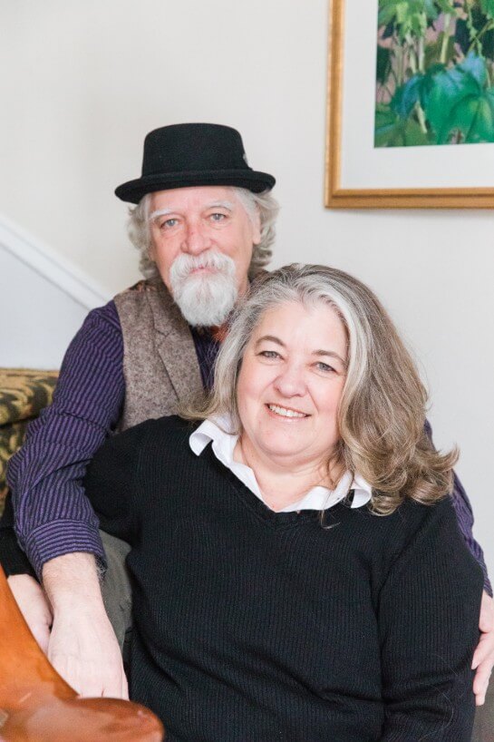 Couple smile at camera while sitting on staircase - man in a hat and woman in a black sweater.