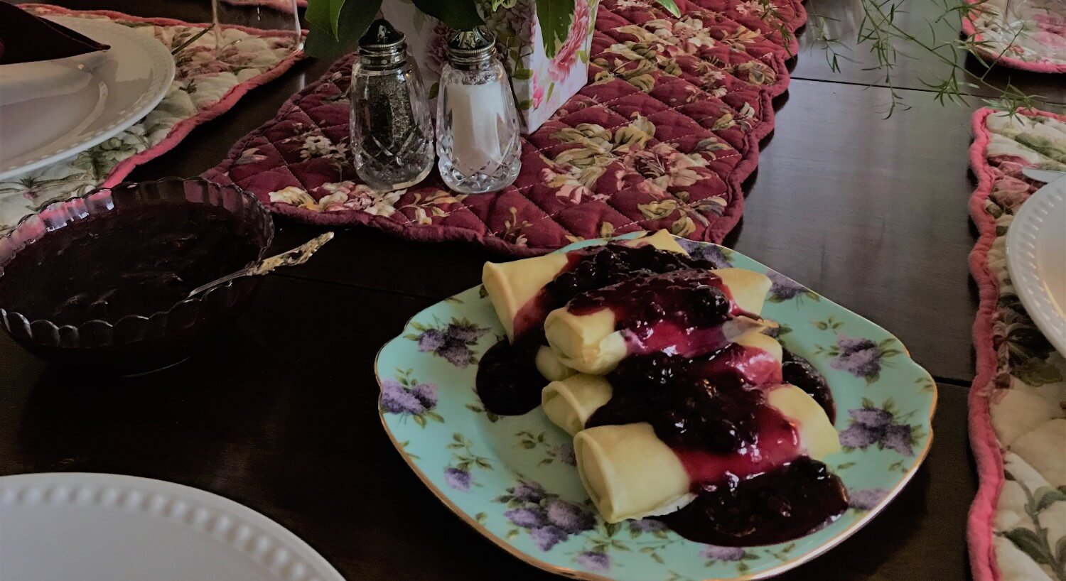 Cheese blintzes covered with blueberry compote on a china plate.