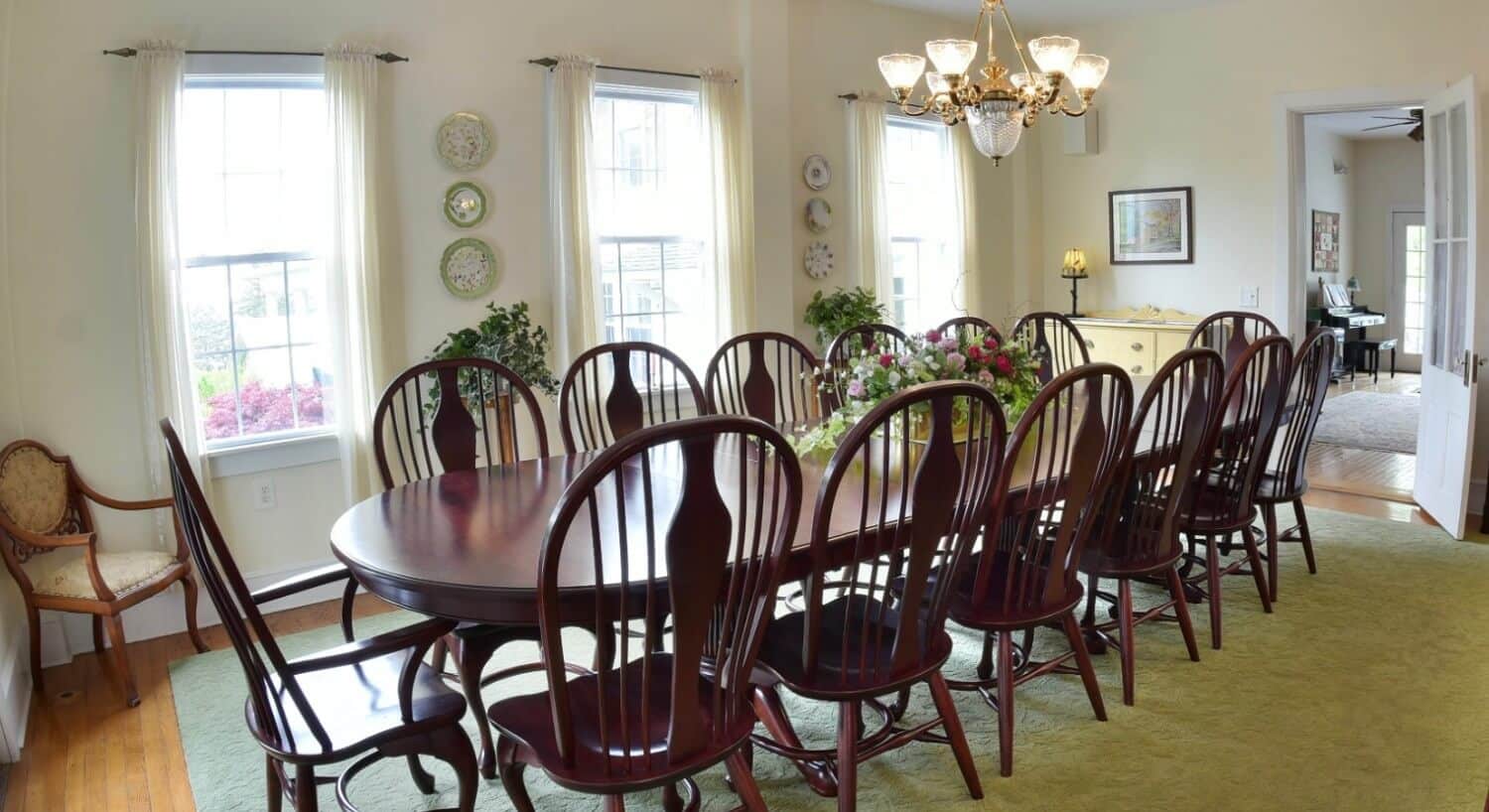 Large dining room with dark cherry wood table and beige curtains by three large windows