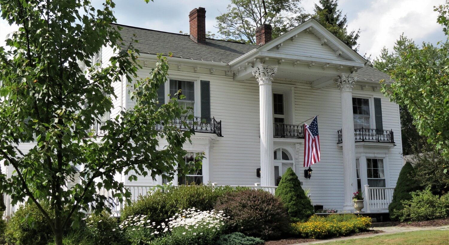 Facade of a large white home with tall pillars and an American flag hanging on the porch