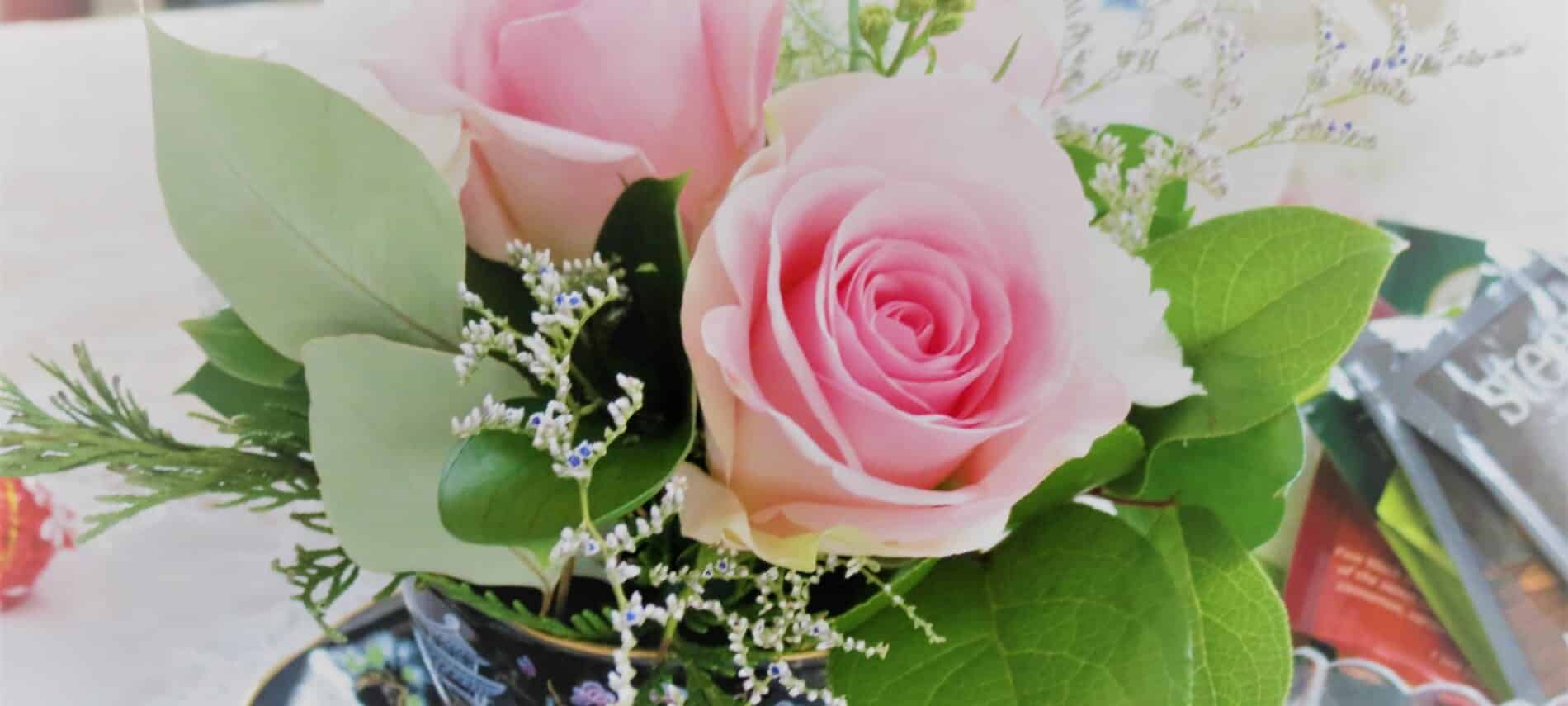 Pink roses with green leaves in a bouquet with baby's breath.