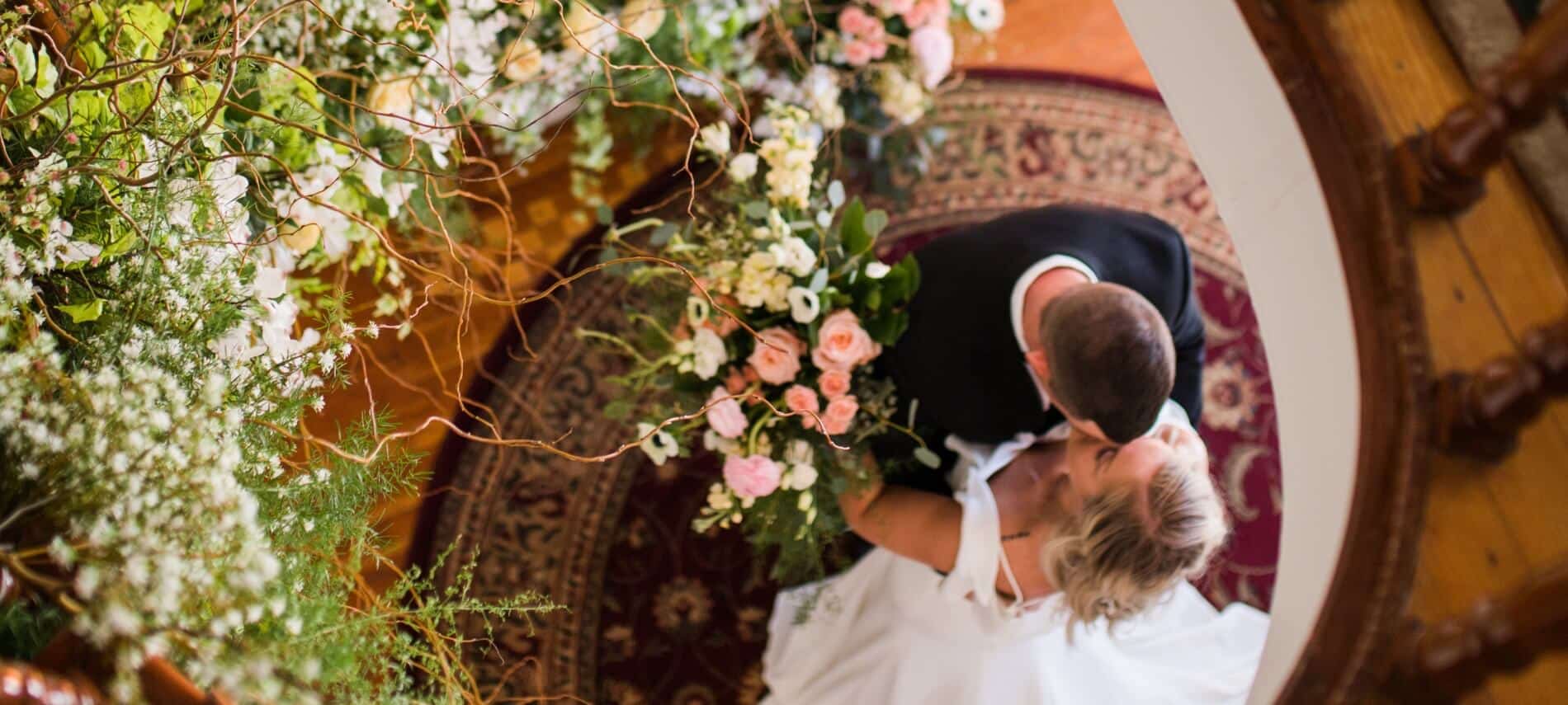 Looking down on a bride and groom embracing at the bottom of a beautiful wooden spiral staircase