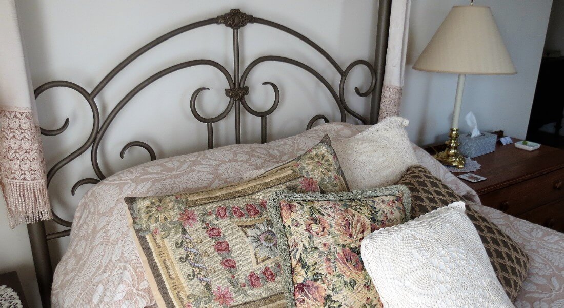 Iron bed is prettily made up with a damask bedspread and needlepoint pillows.