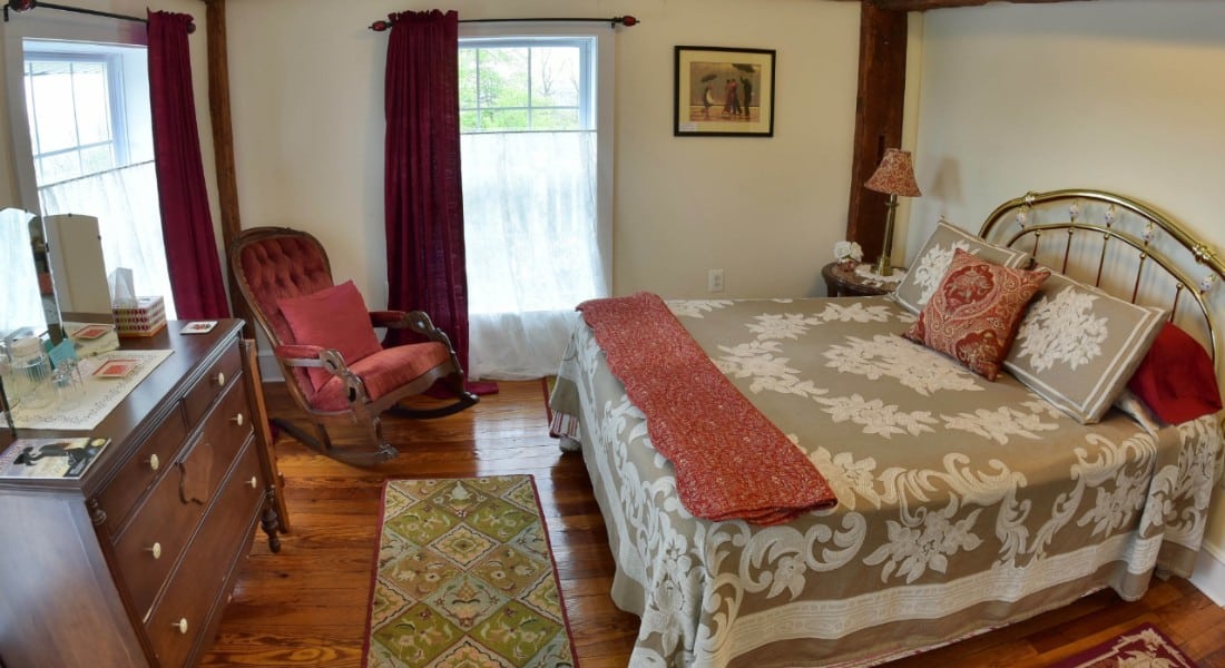 Cozy bedroom furnished with a wooden dresser, queen-sized brass bed and a rocking chair.